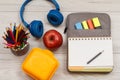 School supplies.. Apple, color pencils, lunch box, headphones and open exercise book on bag-pencil case on gray wooden boards