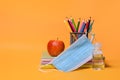 School supplies,an apple , medical masks, sanitizer, on Orange background.Back to school during coronavirus COVID-19 pandemic.Copy