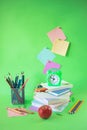 School supplies, apple, a stack of books and an alarm clock on a green background Royalty Free Stock Photo