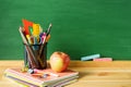 School supplies, pens, pencils in a glass, notebooks, chalk for a blackboard and an apple on a wooden table against the background Royalty Free Stock Photo