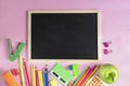 School supplies on pink background with black board. Apple, pen, calculator, paper clip.