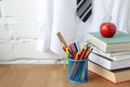 School supplies, a stack of books and an apple on the table against the background of a white shirt with a tie on a hanger, soft Royalty Free Stock Photo