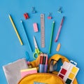 School supplies sticking out of backpack and laid out on blue background Royalty Free Stock Photo