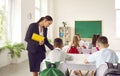 School teacher helping her elementary students who are sitting at desks and writing Royalty Free Stock Photo