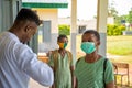 School teacher wearing a lab coat, checking temperature reading of a school pupil