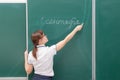 School teacher young woman in a white blouse in the classroom on a green blackboard writes with chalk. translation - September 1 Royalty Free Stock Photo