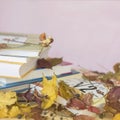 School textbooks, books on table with yellow autumn leaves, against a light pink background with copy space for text
