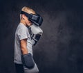 Schoolboy boxer with blonde hair dressed in a white t-shirt wearing visual reality glasses and boxing gloves, workout in Royalty Free Stock Photo