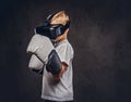 Schoolboy boxer with blonde hair dressed in a white t-shirt wearing visual reality glasses and boxing gloves, workout in Royalty Free Stock Photo