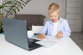 Schoolboy boy blonde learns to read a book during distance learning at home via laptop, concept back to school