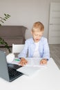 Schoolboy boy blonde learns to read a book during distance learning at home via laptop, concept back to school