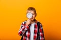 Schoolboy boy looking through a magnifying glass, enlarging his eye on a yellow background