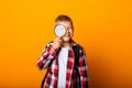 Schoolboy boy looking through a magnifying glass, enlarging his eye on a yellow background