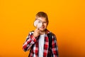 Schoolboy boy looking through a magnifying glass, enlarging his eye on a yellow background