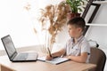 schoolboy boy studying at home doing homework with a laptop writing down the task in a notebook or notepad. junior Royalty Free Stock Photo