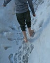 Schoolboy boy walks barefoot through the snow covering the school yard. He is dressed in sweatpants and a thermal shirt. walking t