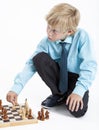 Schoolboy business-style clothing is thinking many moves ahead in chess game, one person on white background