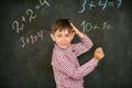 The schoolboy decides on the board the problem with the chalk and thinks over the solution, scratches his head.
