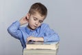 A schoolboy is doing homework at the table. Sadness and tiredness from studying. Gray background Royalty Free Stock Photo