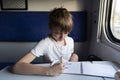 Schoolboy drawing at table in compartment train. Teaching child while traveling