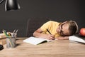 schoolboy in eyeglass laying on table and doing homework at table with lamp books colour pencils and textbook on grey