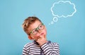 Schoolboy in glasses near blue wall with text cloud with space for your text. Thinking kid. Dream big. Back to school. Royalty Free Stock Photo