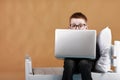 schoolboy in glasses using laptop sitting on bed. Child doing school homework and seriously and tired looking on camera Royalty Free Stock Photo