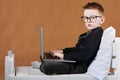 schoolboy in glasses using laptop sitting on bed. Child doing school homework and seriously and tired looking on camera Royalty Free Stock Photo