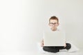 schoolboy in glasses using laptop sitting on bed. Child doing school homework and seriously and tired looking on camera Royalty Free Stock Photo