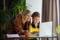 Schoolboy in headphones with mother do a school lessons via computer at home