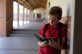 Schoolboy leaning against a wall in an outdoor corridor reading a book at elementary school Royalty Free Stock Photo