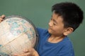 Schoolboy looking globe while standing against green chalkboard in a classroom