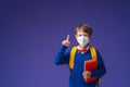 Schoolboy in mask, in uniform with book and backpack on purple background