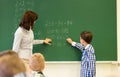 Schoolboy with math teacher writing on chalk board