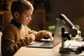 schoolboy with a microscope and laptop on his workplace. Doing homework in biology. Process of teaching and scientific Royalty Free Stock Photo
