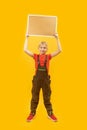 Schoolboy in overalls holds blankboard above his head. Full-length portrait on yellow background. Place for text