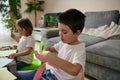 Schoolboy and preschool girl focused on creativity. Drawing and cutting shapes from color paper at home