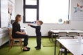 Schoolboy at primary school presenting a gift to his female teacher in a classroom, full length, side view Royalty Free Stock Photo