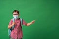 Schoolboy in protective mask, standing against background of a green Board