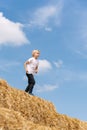 Schoolboy runs on dry hay. Blond child in village on large haystack against blue sky. Summer vacation