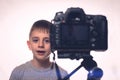 Schoolboy is saying something on a camcorder. Young video blogger. Camera in the foreground