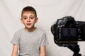 Schoolboy is saying something on a camcorder. Young video blogger. White background