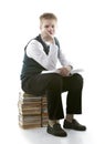 The schoolboy in a school uniform sits on a pack of books, with the opened book in hands