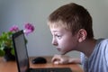 Schoolboy sits his nose buried in a laptop. Internet and preschooler