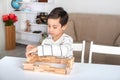 A schoolboy sits on the table and plays in a wooden cons