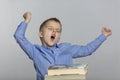 A schoolboy sits at a table with books, yawns and sips. Gray background