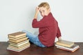 The schoolboy sits on the table near the books and holds his head with his hand, turning his back