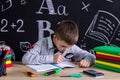 Schoolboy sitting at the desk with books, school supplies, searching the text in the exercise book by means of