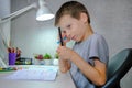 A schoolboy is sitting at a table with felt-tip pens in hand. The child does homework, homework. A boy with a pensive Royalty Free Stock Photo