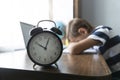 Schoolboy sleep on desk by laptop, clock shows time at front.